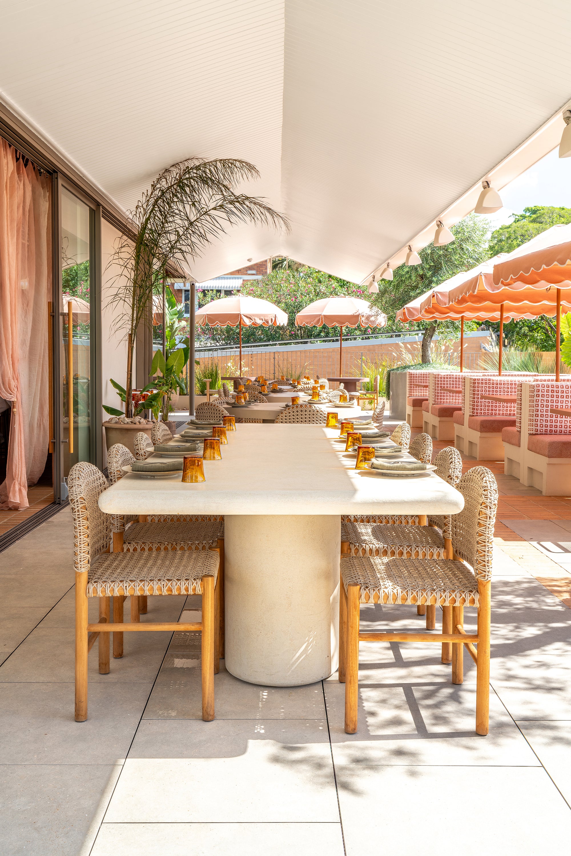 Mukalla dining table viewed from the front on a rooftop terrace with woven chairs soft neutral tones and sunlit outdoor dining ambience