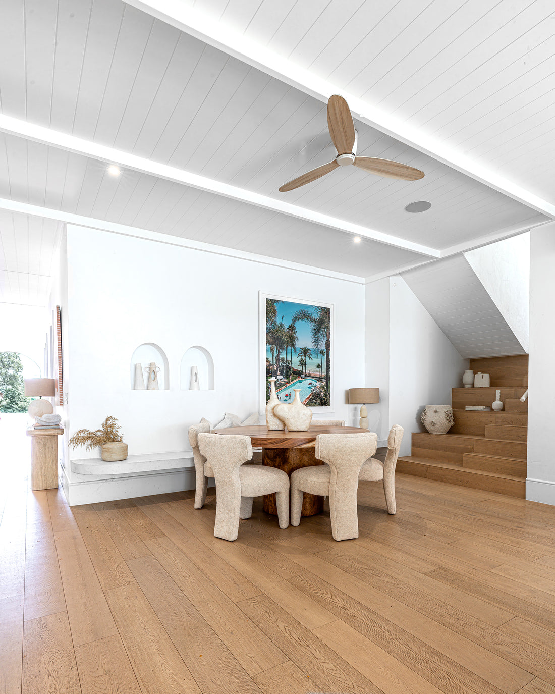 A contemporary coastal dining space featuring a sculptural wooden table, plush boucle dining chairs, and minimalist décor, creating a serene and inviting atmosphere with warm natural textures