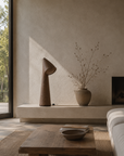 Nhara table lamp with a sculptural paper mache base and angled shade styled on a minimalist hearth in a warm natural living room.