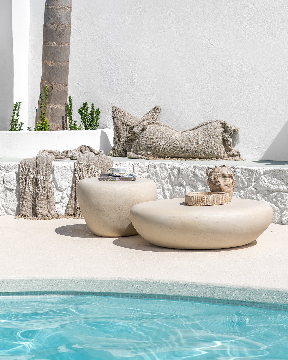 Nomara Side Table and Coffee Table in Driftstone styled beside a swimming pool.