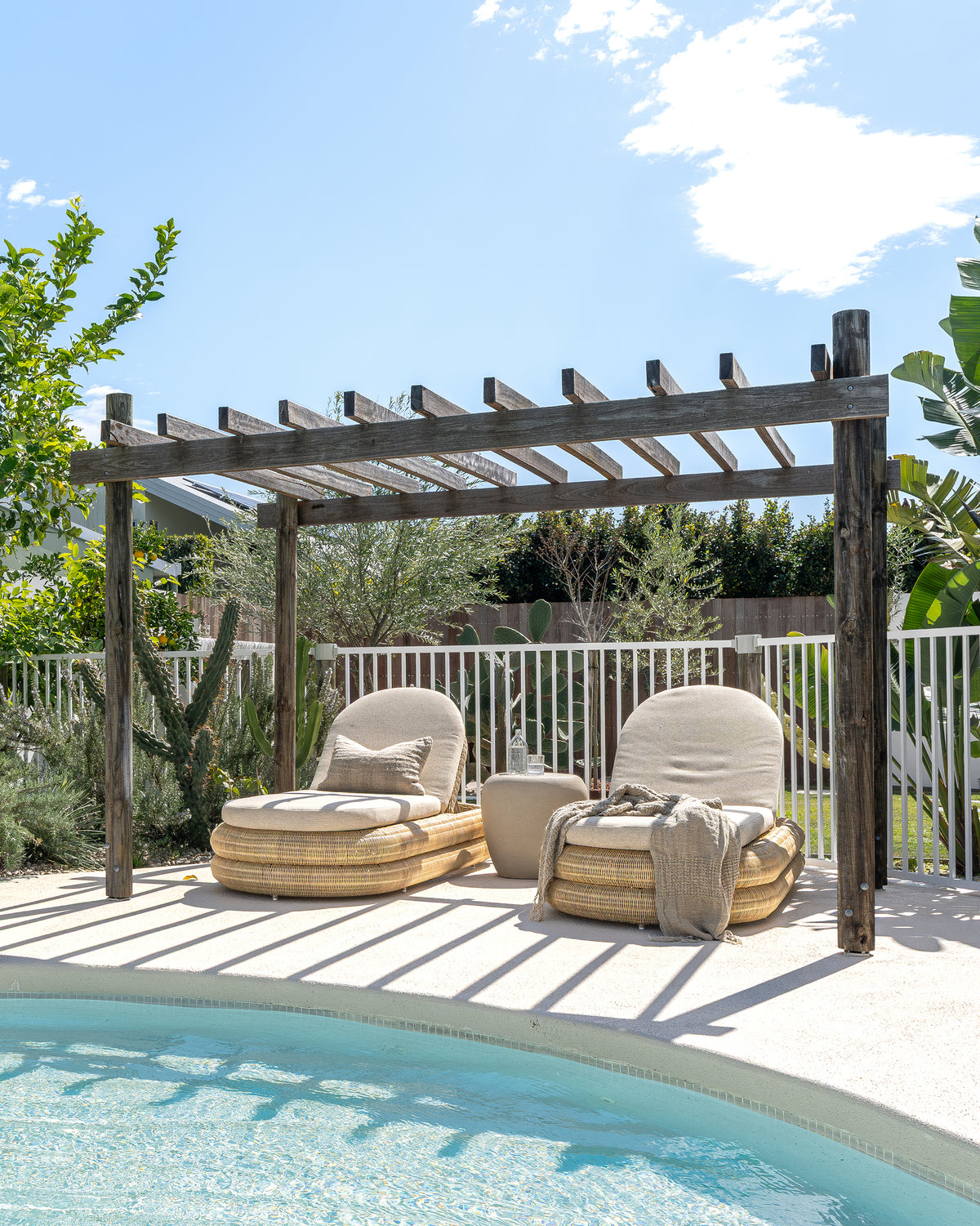 Nomara Side Table in Driftstone positioned between two Satori Outdoor Sun Loungers beside a swimming pool.