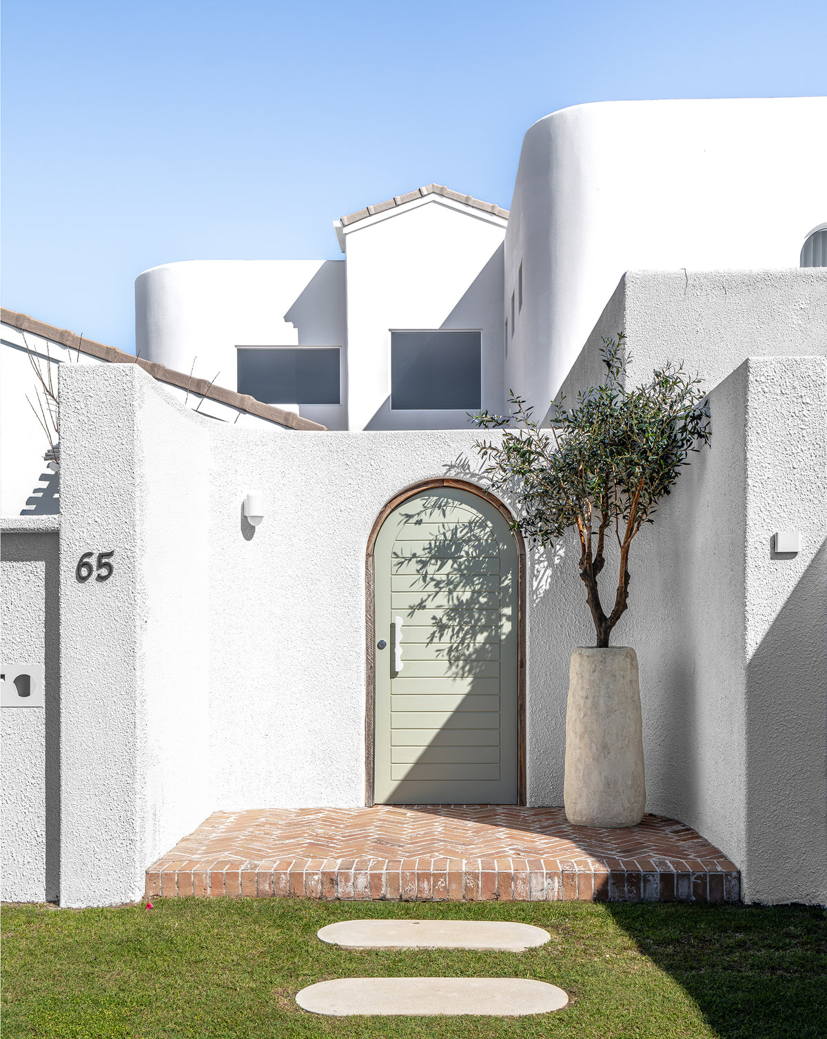 Nusa Palm Planter styled with an olive tree beside an arched entrance of a white Mediterranean inspired home.
