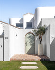 Nusa Palm Planter styled with an olive tree beside an arched entrance of a white Mediterranean inspired home.