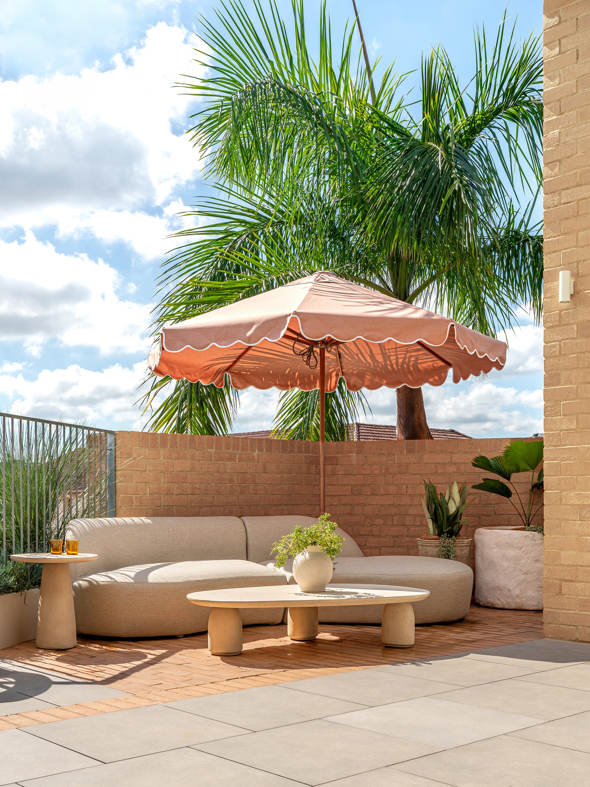 Oasis sofa paired with Maaru planter in a sunlit rooftop lounge with soft curved seating warm brick textures and lush greenery creating a relaxed outdoor retreat