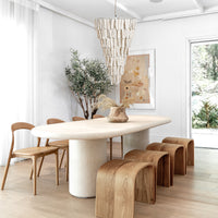 A beautifully styled dining room with a sculptural stone dining table, curved wooden stools, and minimalist wooden chairs, featuring an organic cascading pendant light and soft neutral décor