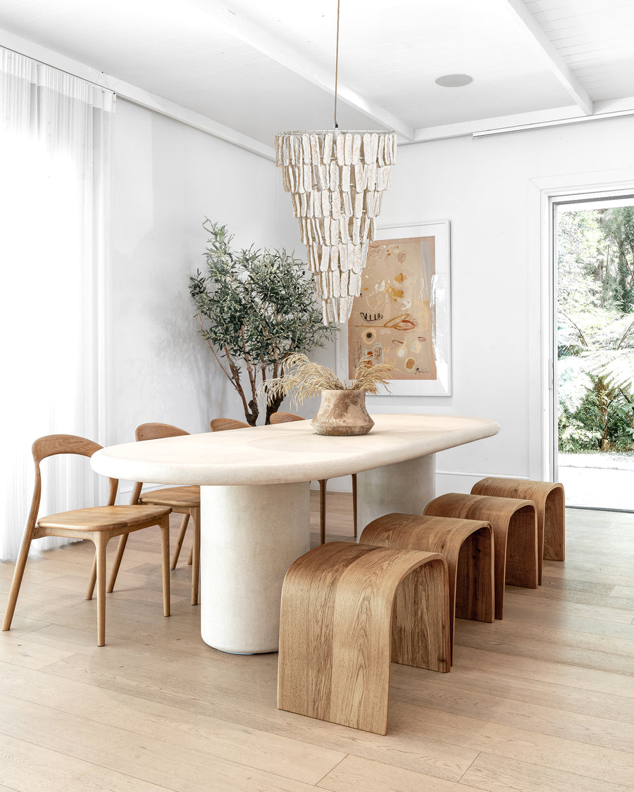 A beautifully styled dining room with a sculptural stone dining table, curved wooden stools, and minimalist wooden chairs, featuring an organic cascading pendant light and soft neutral décor