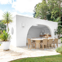 Outdoor dining setting featuring a round concrete dining table paired with woven dining chairs, styled under a modern white archway for a serene alfresco entertaining space