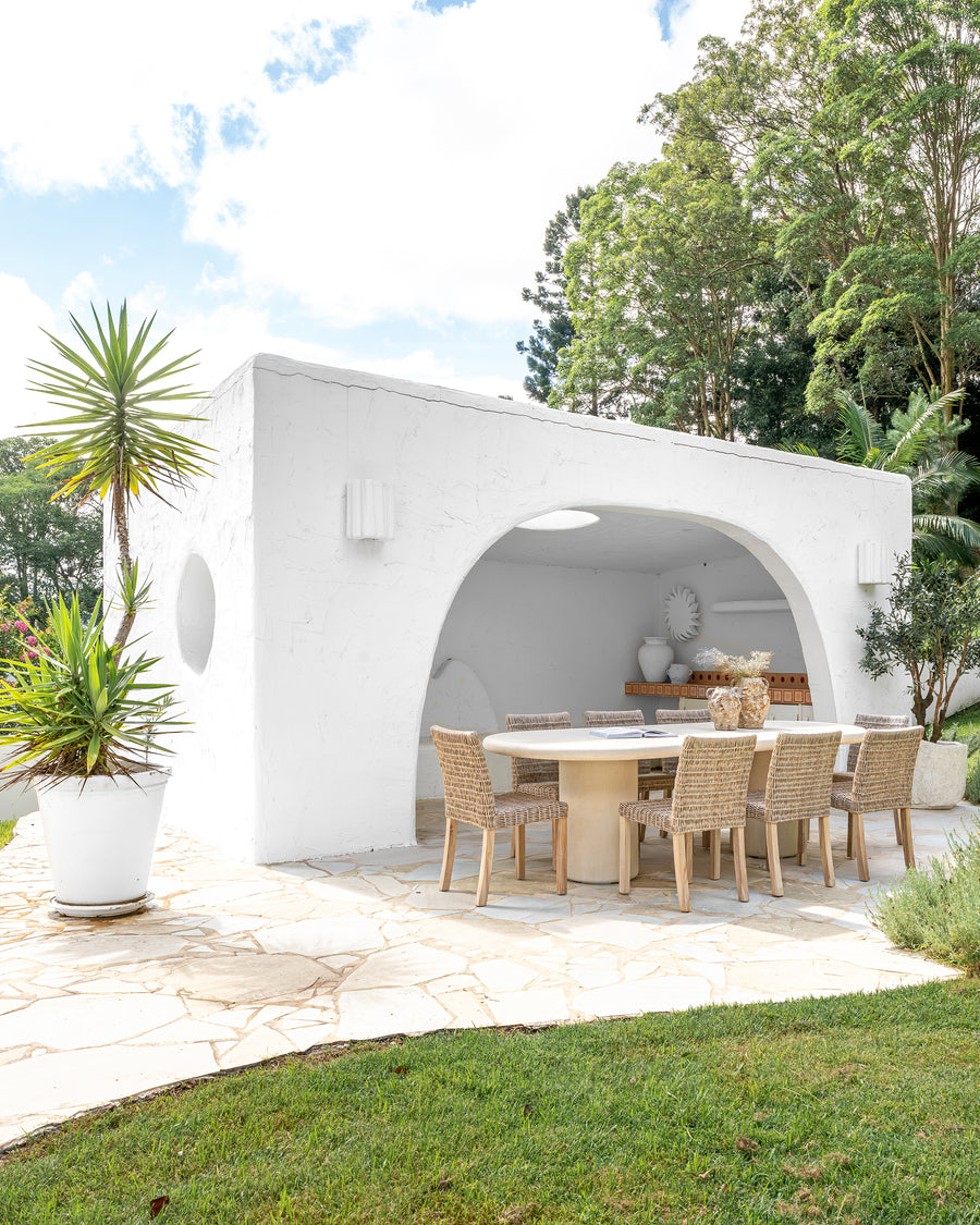 Outdoor dining setting featuring a round concrete dining table paired with woven dining chairs, styled under a modern white archway for a serene alfresco entertaining space