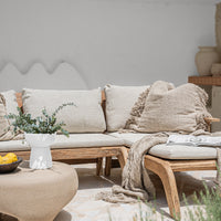 A beautifully curated outdoor lounge setting featuring a handcrafted teak sofa with plush neutral cushions, textured throw blankets, and organic décor, creating a relaxed resort-style ambiance.