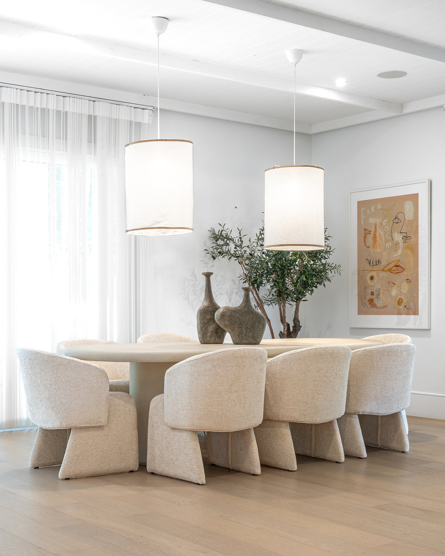 Elegant dining room featuring a sculptural plaster dining table surrounded by upholstered dining chairs in a neutral palette, complemented by soft linen pendant lights and artisanal decor