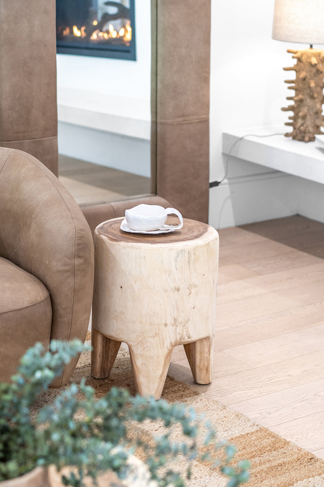 Raw teak side table styled beside a leather lounge, featuring a handcrafted ceramic cup and saucer, with a coral-inspired table lamp in the background, creating a warm and organic living space