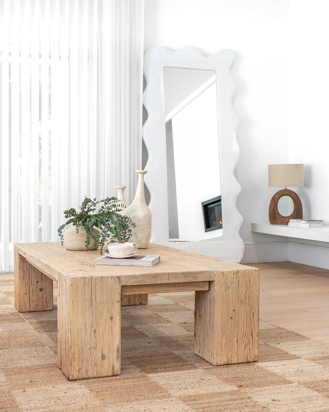 Uniqwa Collections a reclaimed wood coffee table styled with ceramic vases, greenery, and a sculptural cup, set in a bright living space featuring a statement mirror, neutral tones, and natural textures for a modern organic aesthetic