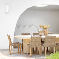 Round concrete dining table paired with woven dining chairs, styled under a white archway with natural vases and dried foliage, creating a tranquil alfresco dining space.