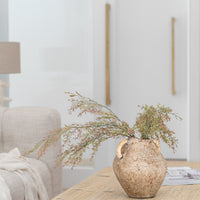 A rustic ceramic vase with woven handles, filled with dried foliage, sits atop a natural timber coffee table in a serene living space. Styled with organic textures and neutral tones, perfect for modern interiors