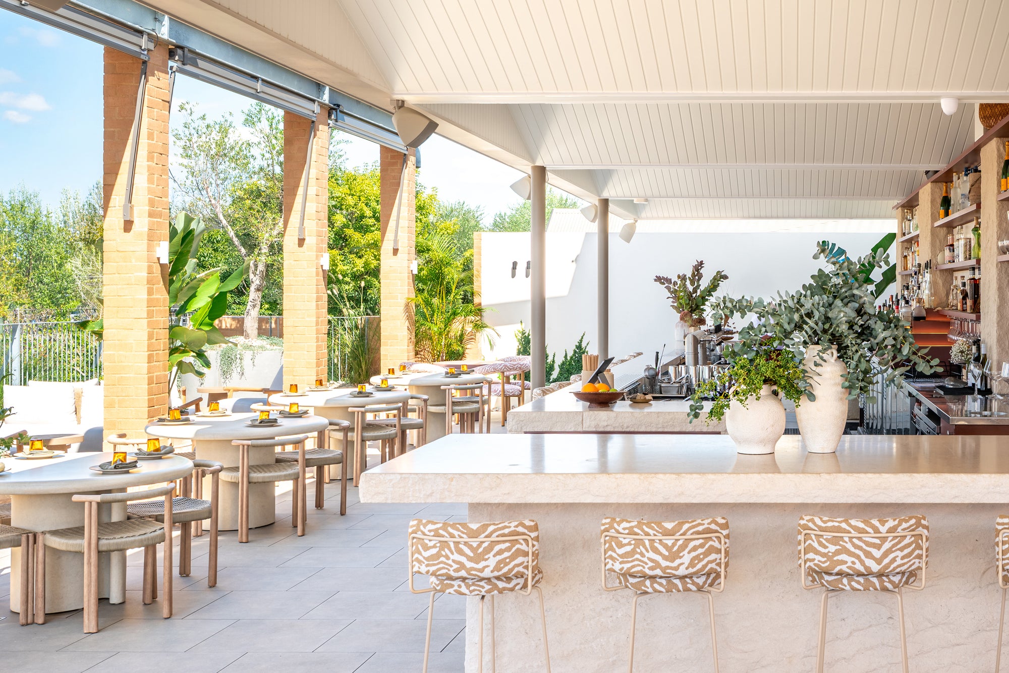 Salalah dining tables arranged beside a light filled rooftop bar with timber chairs soft stone finishes and greenery creating a relaxed open air dining atmosphere