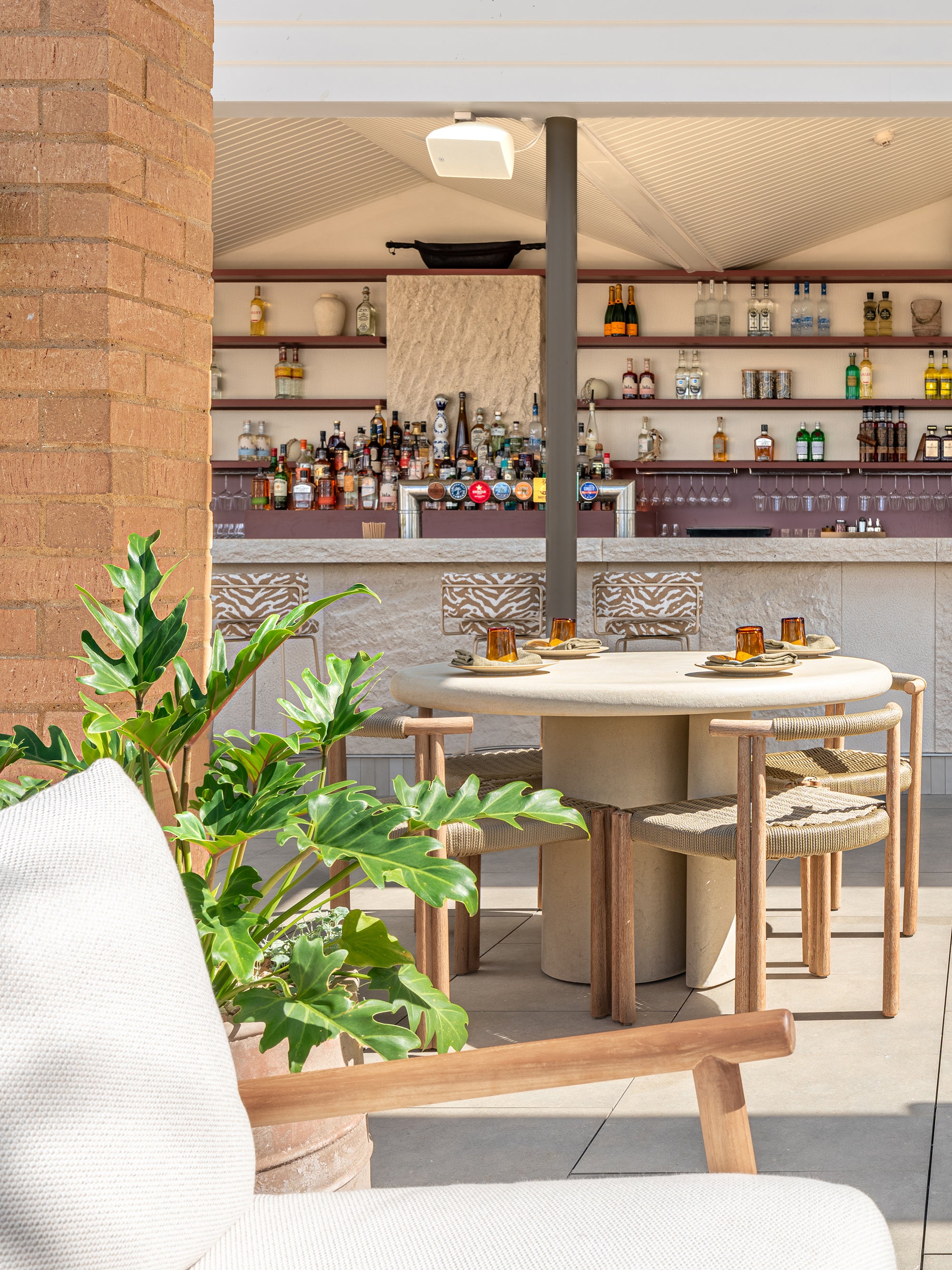 Salalah dining table styled in an open air rooftop bar setting with woven timber chairs warm stone finishes and lush greenery creating a relaxed coastal atmosphere
