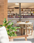 Salalah dining table styled in an open air rooftop bar setting with woven timber chairs warm stone finishes and lush greenery creating a relaxed coastal atmosphere