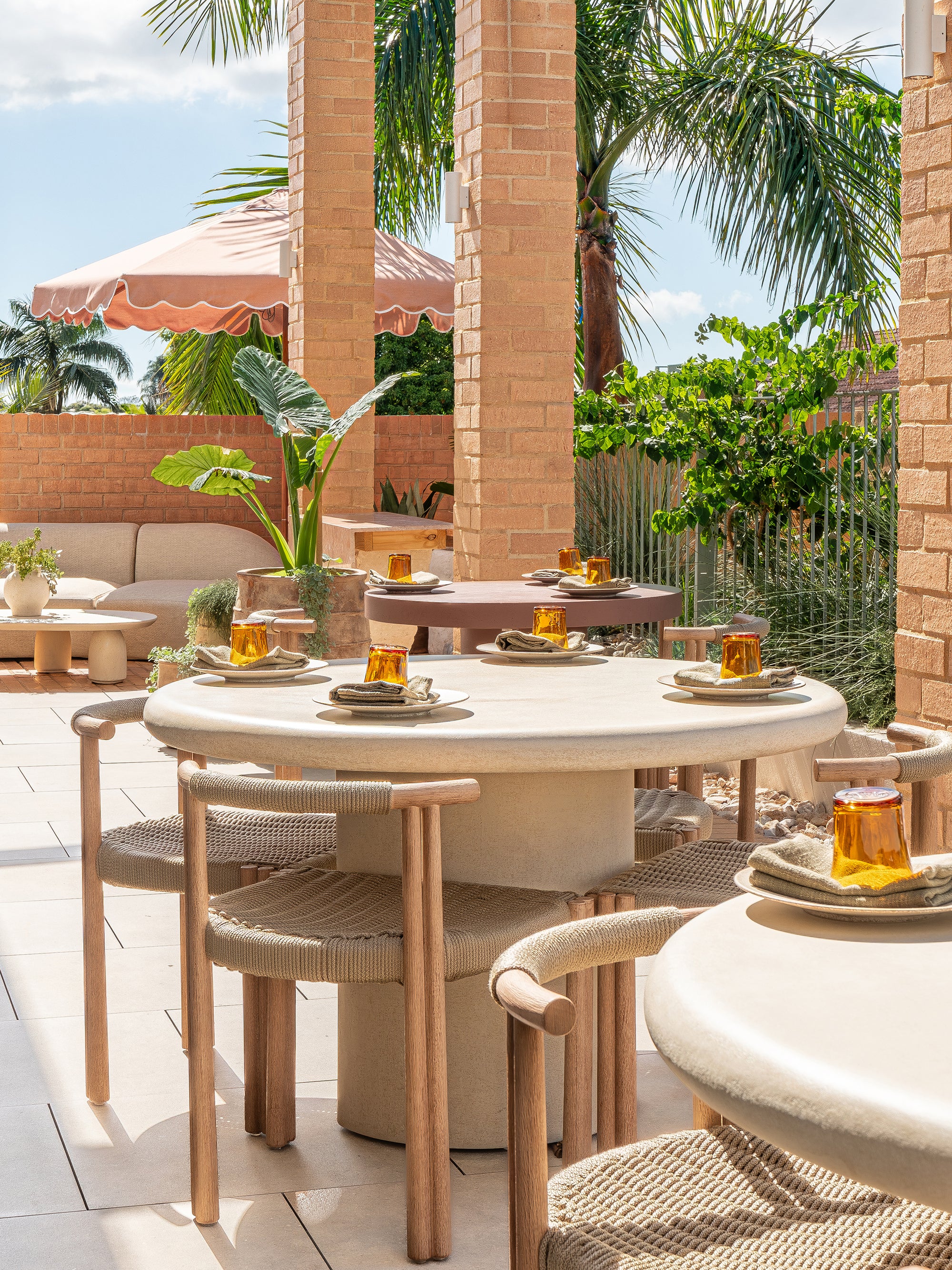 Salalah dining table styled on a rooftop terrace with woven chairs soft neutral finishes and surrounding tropical greenery creating a warm open air dining setting
