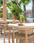 Salalah dining table arranged across a sunlit rooftop setting with woven chairs warm brick architecture and lush tropical planting creating a relaxed outdoor dining atmosphere