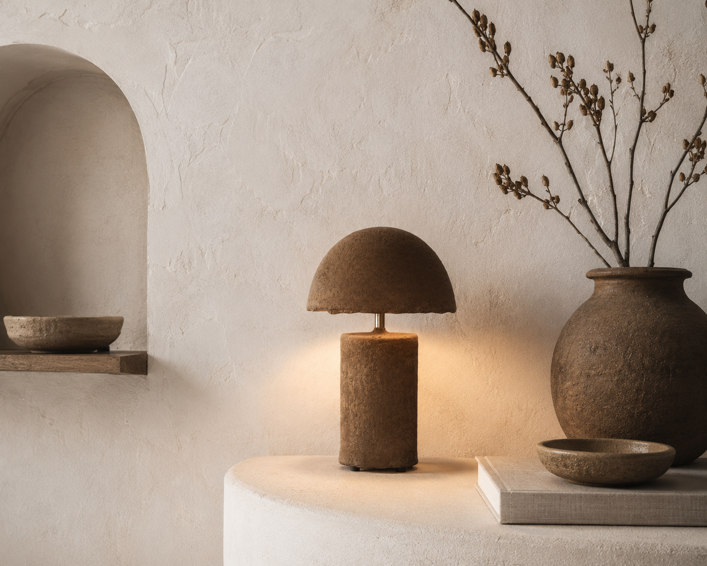 Small Samrah table lamp with textured brown paper mache and dome shade casting a warm ambient glow in a natural styled interior.