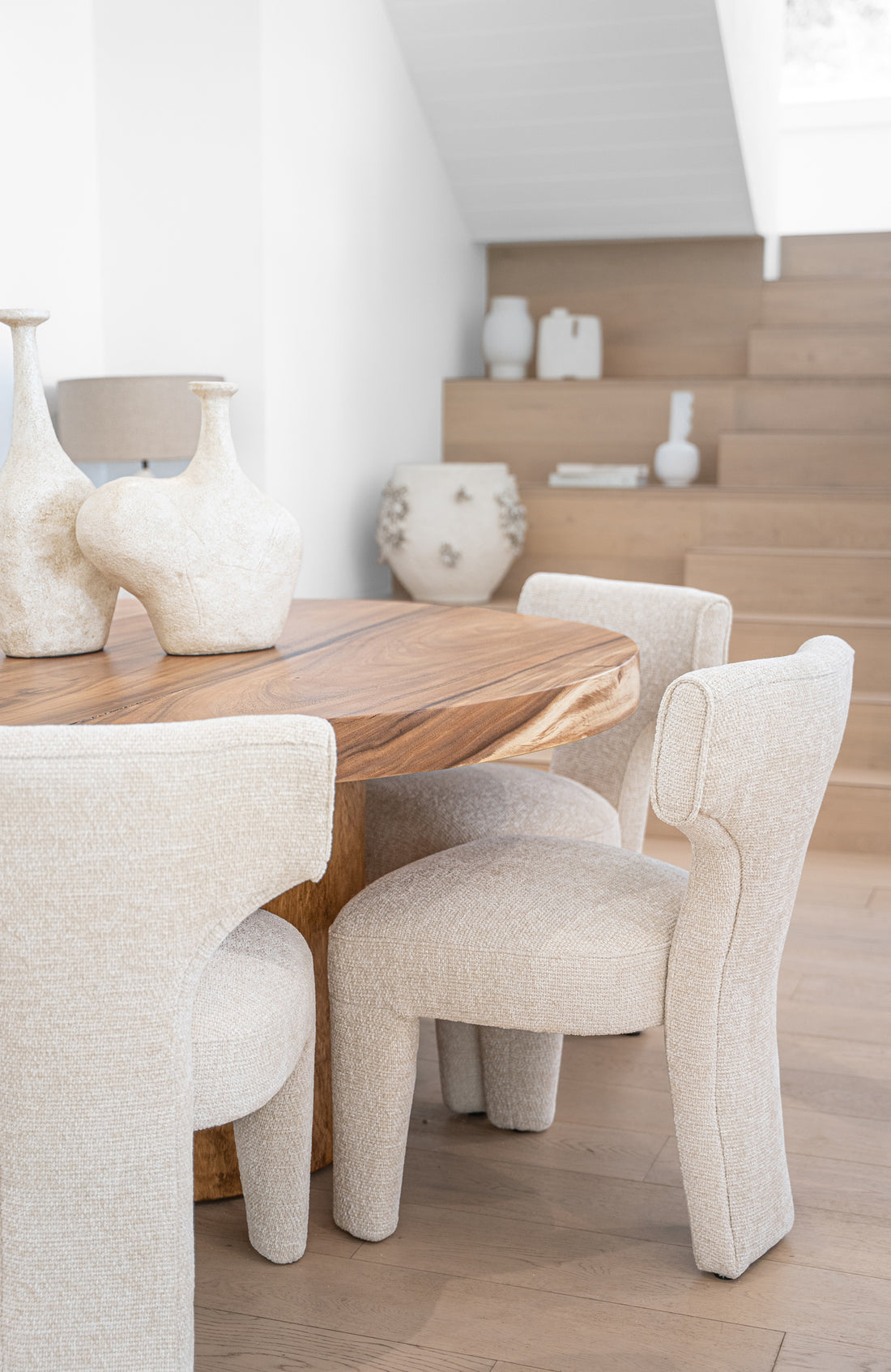 A luxurious dining setting featuring a solid wood live-edge dining table paired with sculptural boucle dining chairs. The organic textures and soft neutral tones create a warm, contemporary aesthetic