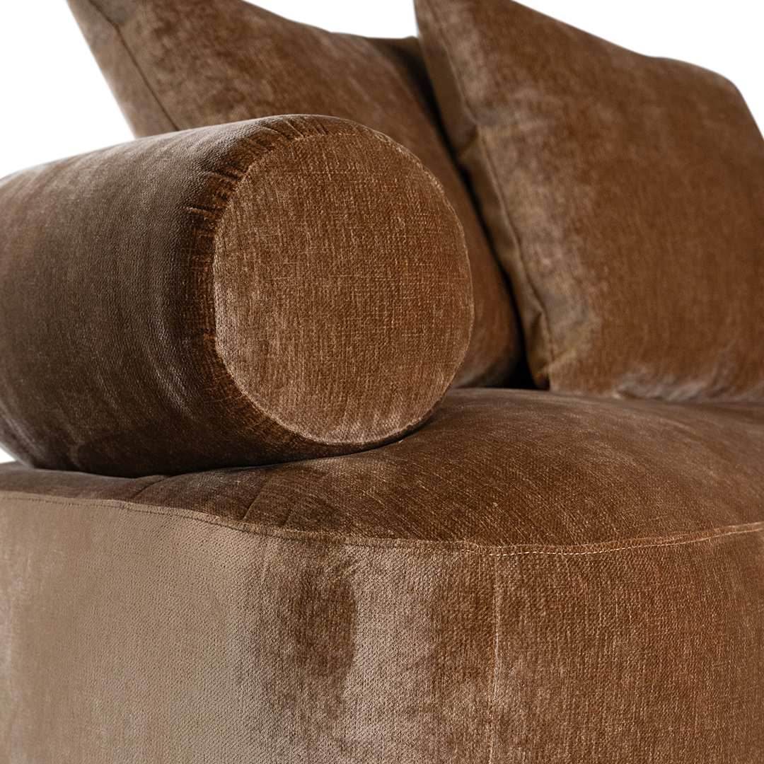 Soneva  one seater sofa in bronze fabric featuring a soft curved silhouette with round bolster cushions and plush back pillows.