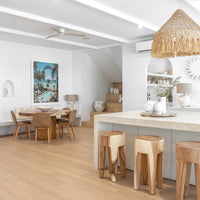 Teak bar stools paired with a stone kitchen island, complemented by a woven rattan pendant light and a round timber dining table with leather dining chairs, creating a warm and inviting modern dining space