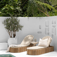 Luxury outdoor teak sun loungers with plush cushions, set against a white Mediterranean-style backdrop with lush greenery, creating a serene poolside retreat