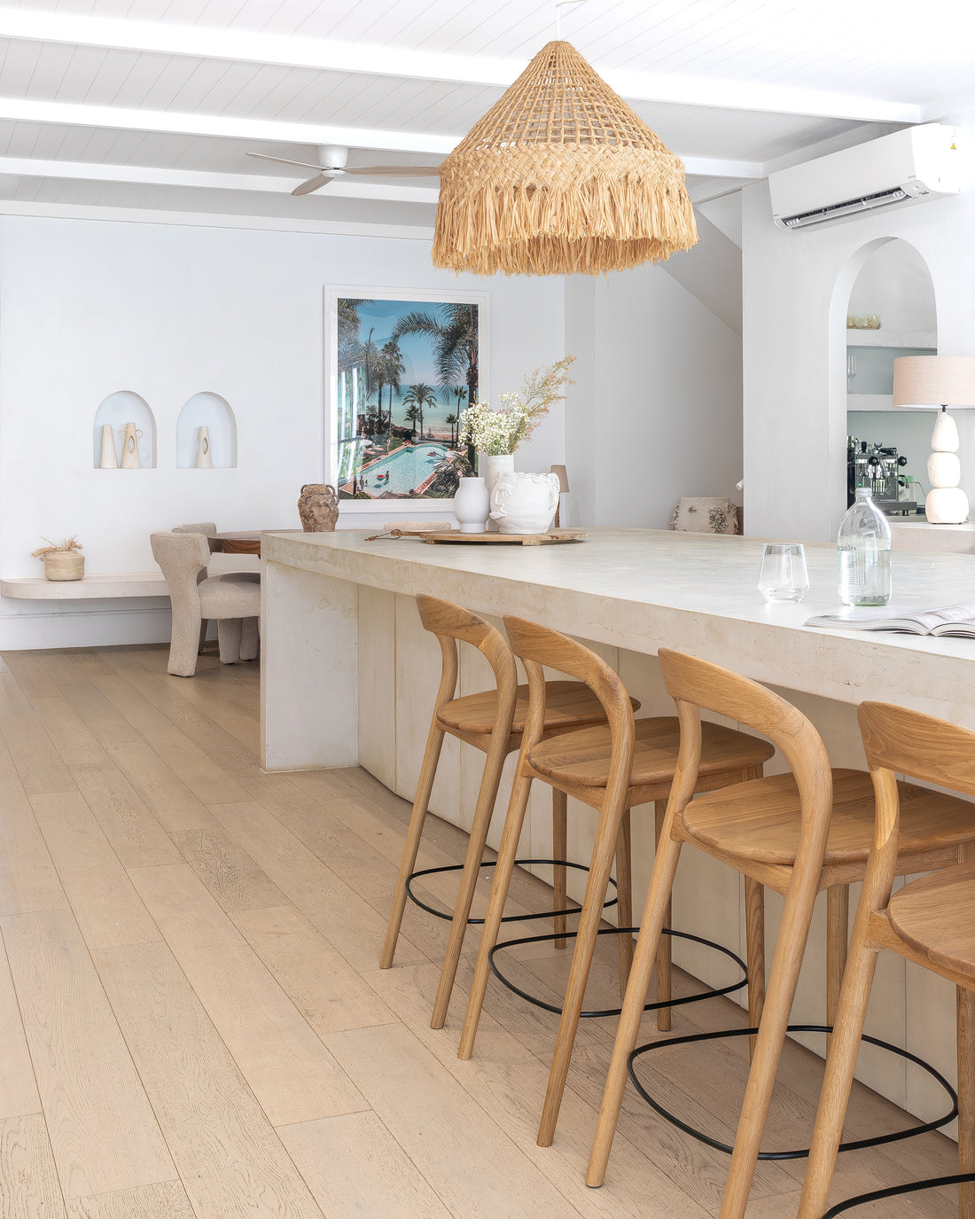 Timber bar stools paired with a stone kitchen island, styled with organic ceramics and a woven pendant light, creating a warm and textural open-plan living space