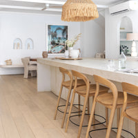 Timber bar stools paired with a stone kitchen island, styled with organic ceramics and a woven pendant light, creating a warm and textural open-plan living space