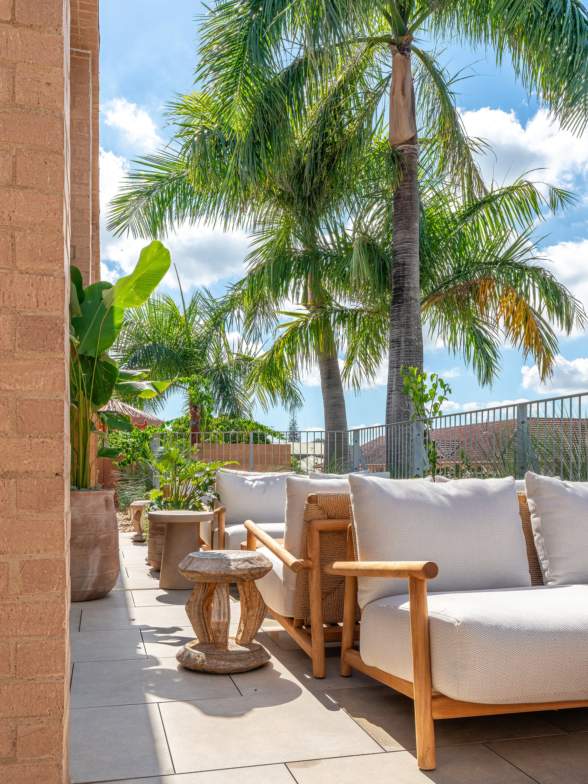 Tsuana stool styled on a sunlit rooftop terrace with timber lounge seating soft neutral cushions and surrounding tropical greenery creating a relaxed outdoor retreat
