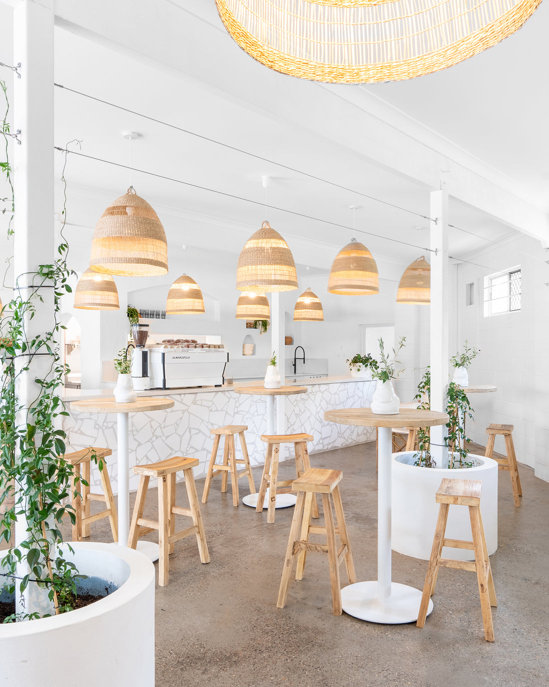 Uniqwa bar table setting with white pedestal base and natural teak bar stools in a stylish resort-inspired commercial venue.