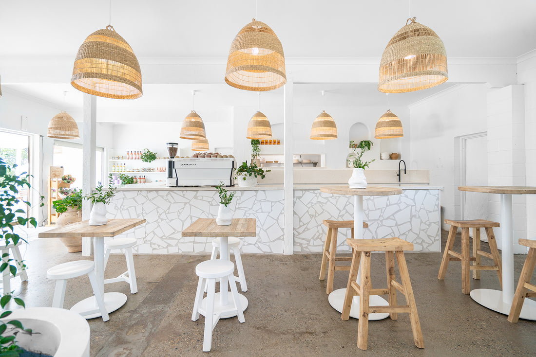 Uniqwa bar table setting with white pedestal base and natural teak bar stools in a stylish resort-inspired commercial venue.