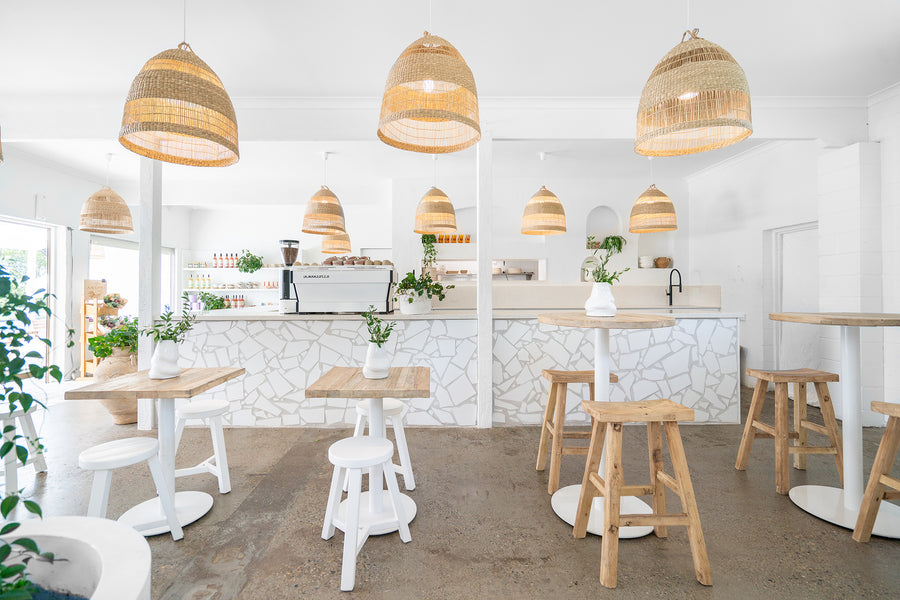 Uniqwa bar table setting with white pedestal base and natural teak bar stools in a stylish resort-inspired commercial venue.