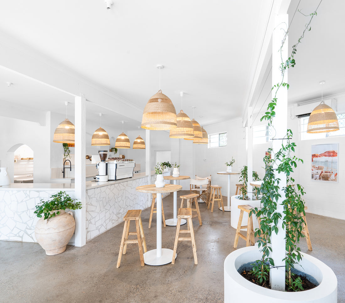 Uniqwa bar table setting with white pedestal base and natural teak bar stools in a stylish resort-inspired commercial venue.