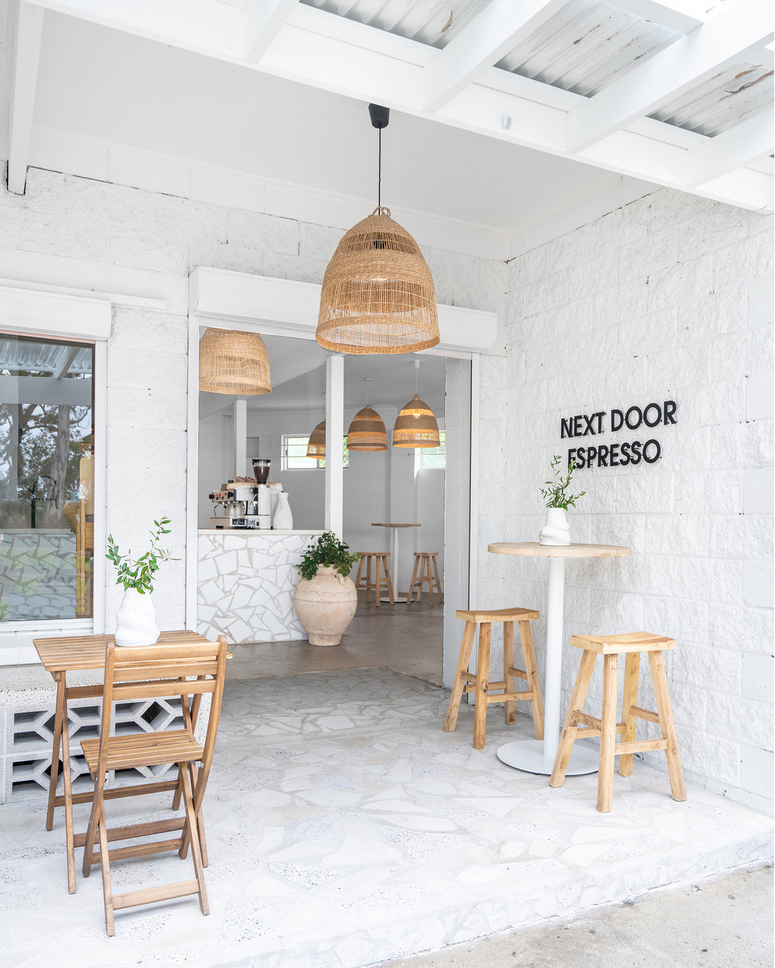 Uniqwa bar table setting with white pedestal base and natural teak bar stools in a stylish resort-inspired commercial venue.