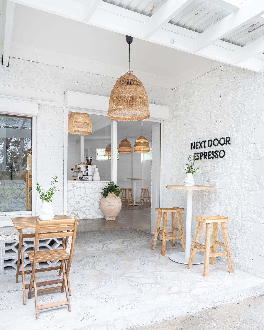 Uniqwa bar table setting with white pedestal base and natural teak bar stools in a stylish resort-inspired commercial venue.