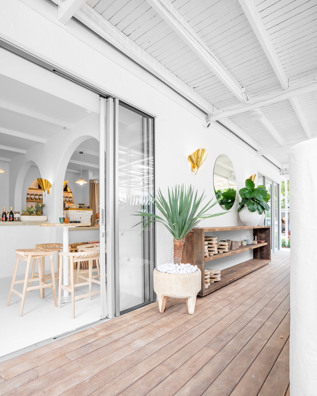 Uniqwa bar table setting with white pedestal base and natural teak bar stools in a stylish resort-inspired commercial venue.