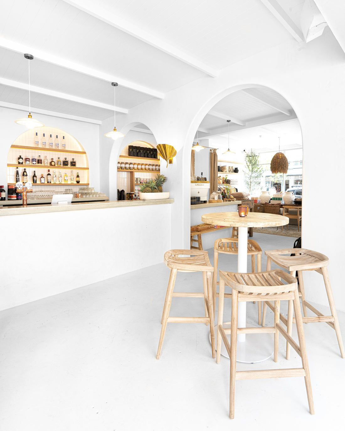 Uniqwa bar table setting with white pedestal base and natural teak bar stools in a stylish resort-inspired commercial venue.