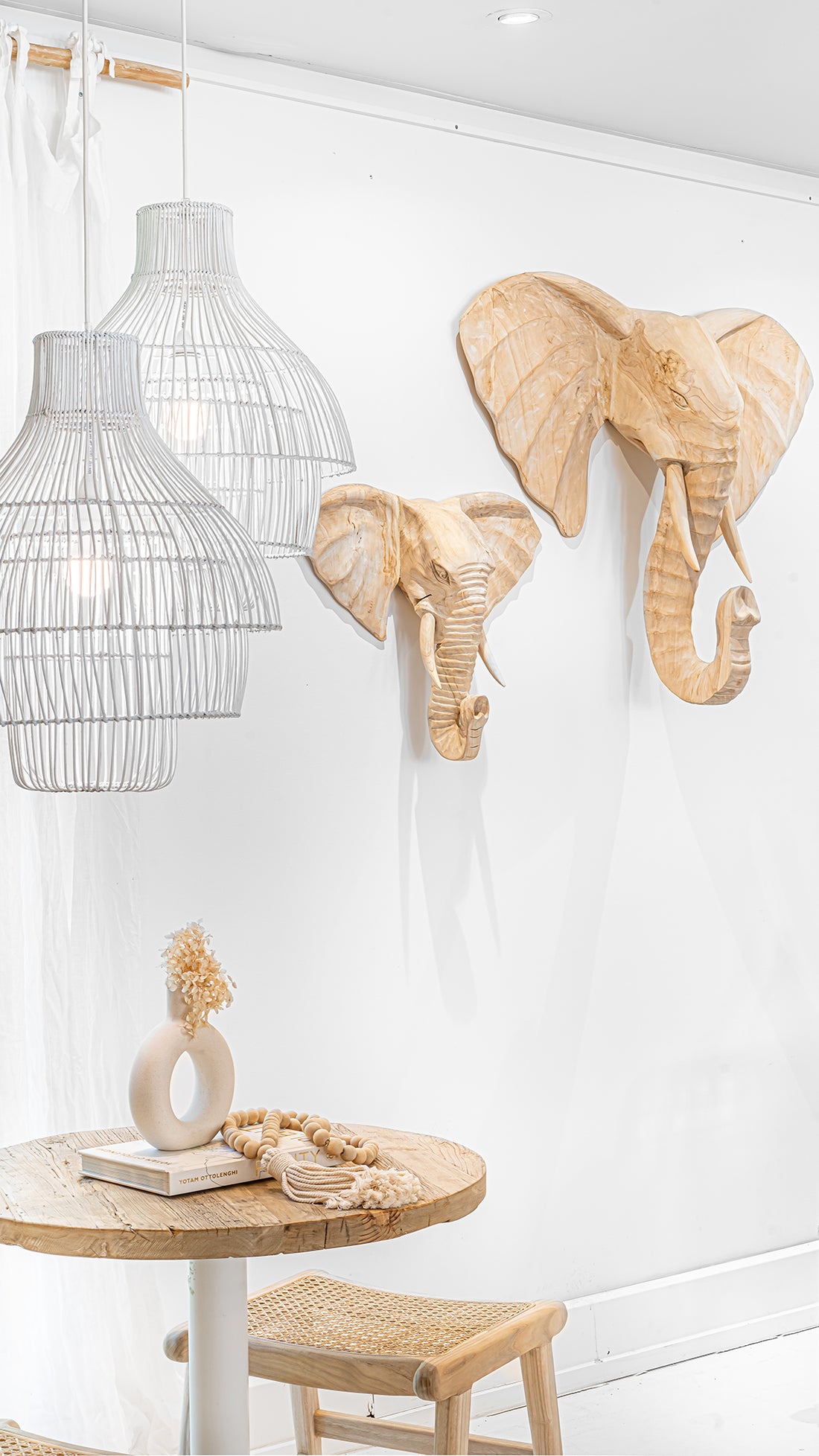 Uniqwa Collections Brunswick Bar Table with white base styled with cane stool seating, wall-mounted elephant head sculptures, and white wire pendant lighting for a natural, textural interior look.