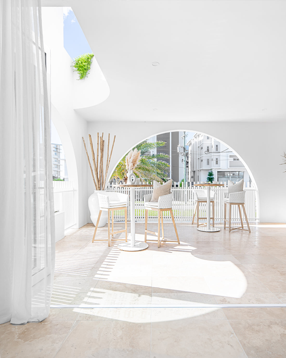 Uniqwa Collections Brunswick Bar Tables with white base styled on a sun-drenched arched terrace, paired with woven bar stools and soft neutral cushions for a refined outdoor hospitality space.