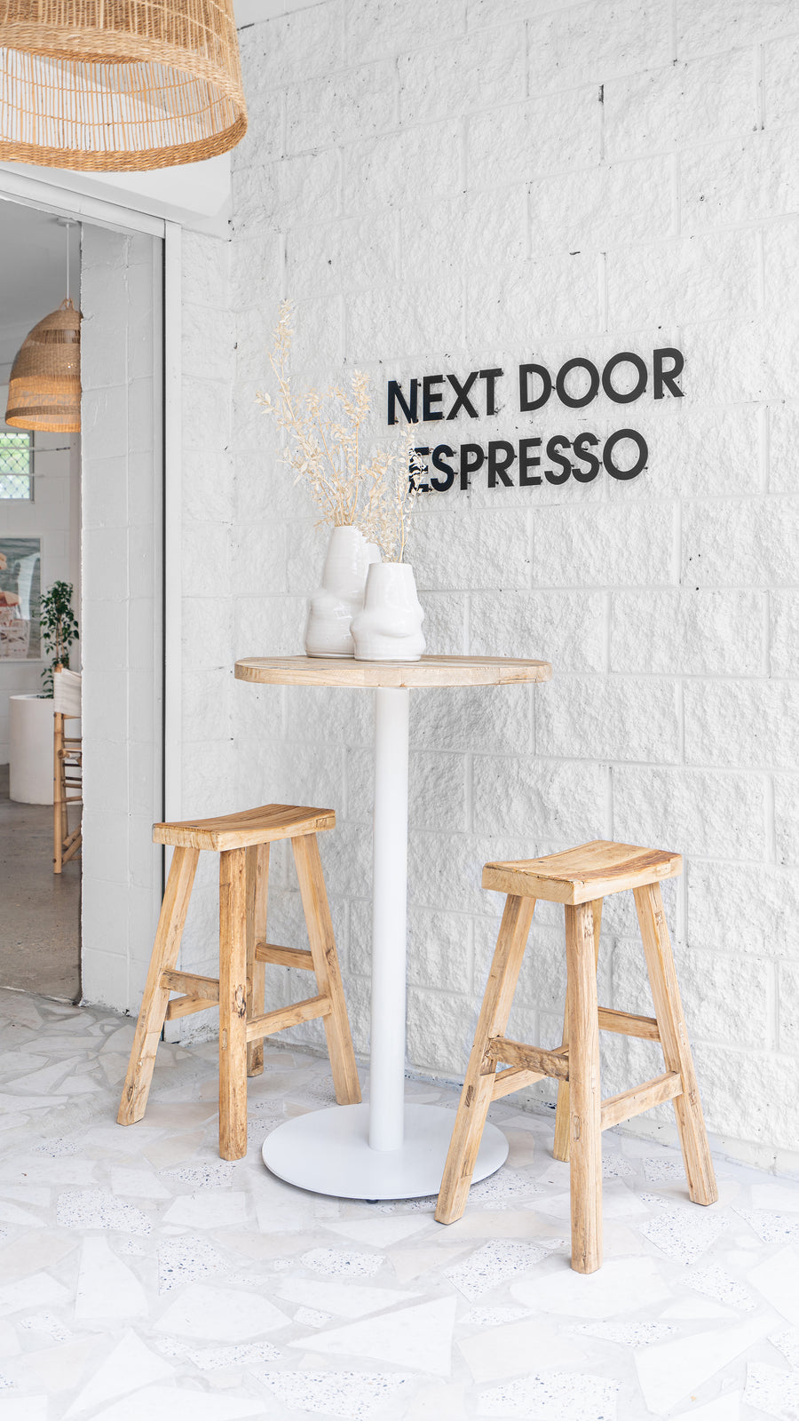 Uniqwa Collections Brunswick Bar Table with white base styled outside Next Door Espresso café with rustic timber stools and ceramic vases for a relaxed, coastal setting.
